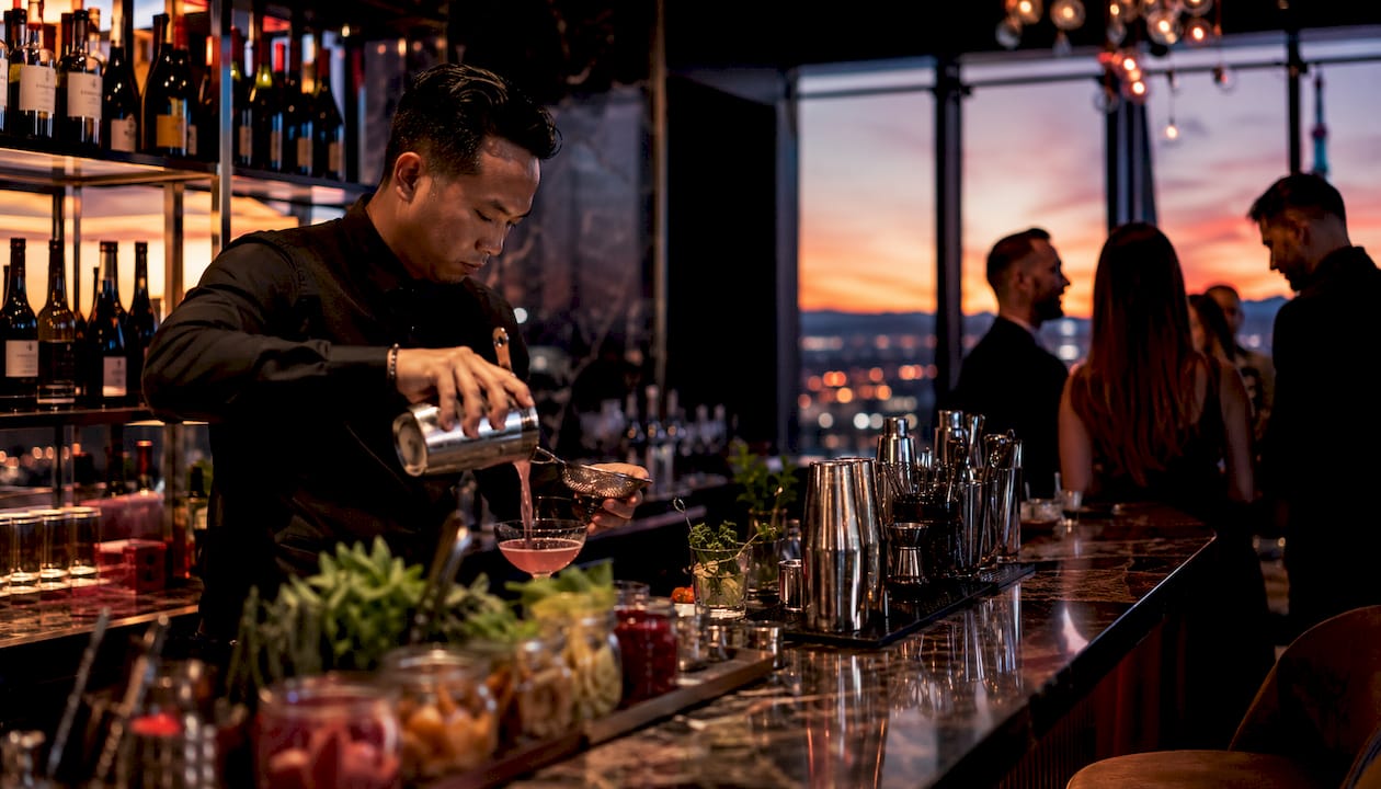 Bartender mixing cocktails at illuminated beverage station