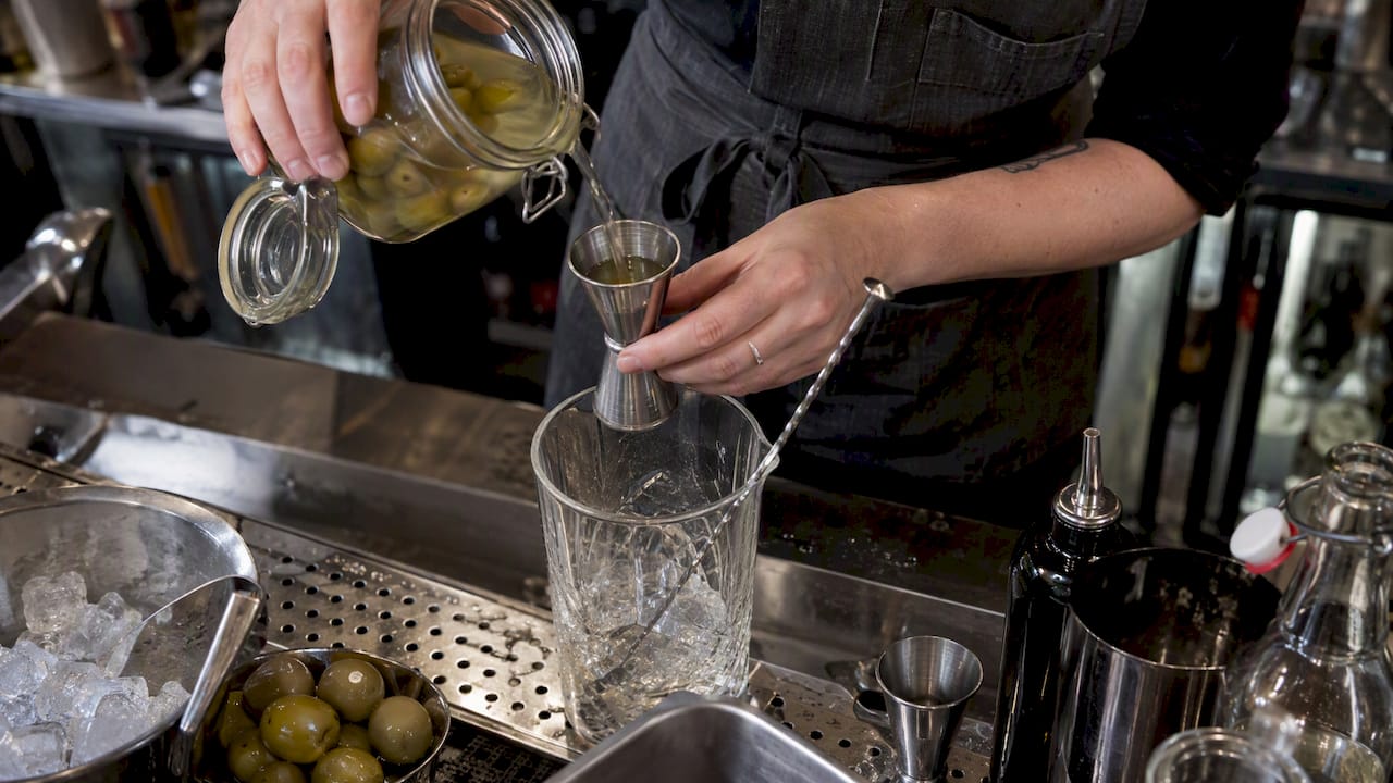 Bartender measuring olive brine for martini